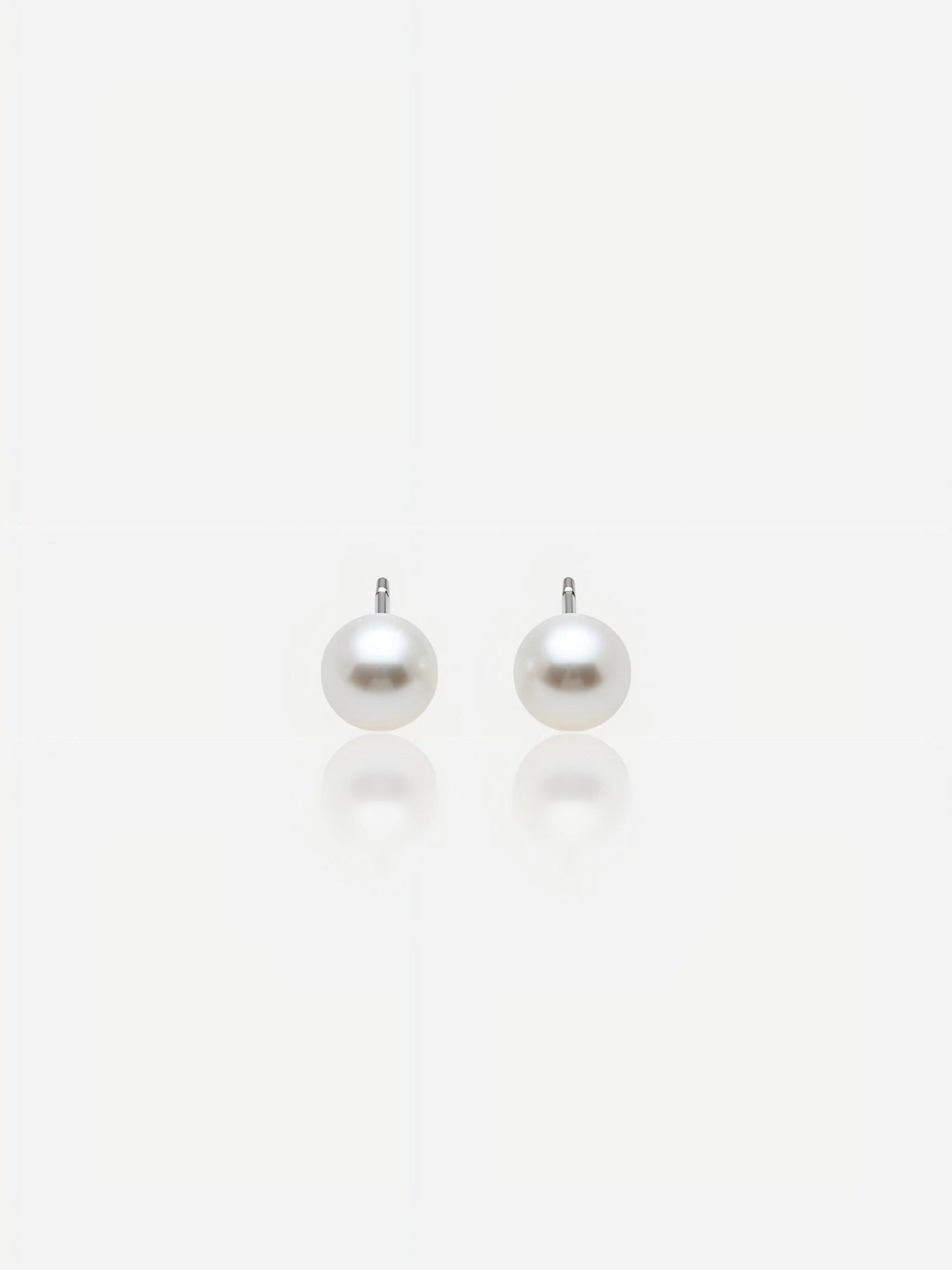 Close-up of Pearltide Aurora flawless round pearl jewelry earrings with brilliant Akoya-like mirror luster and S925 sterling silver settings on a white background with soft reflections, elegant minimalist bridal jewelry.