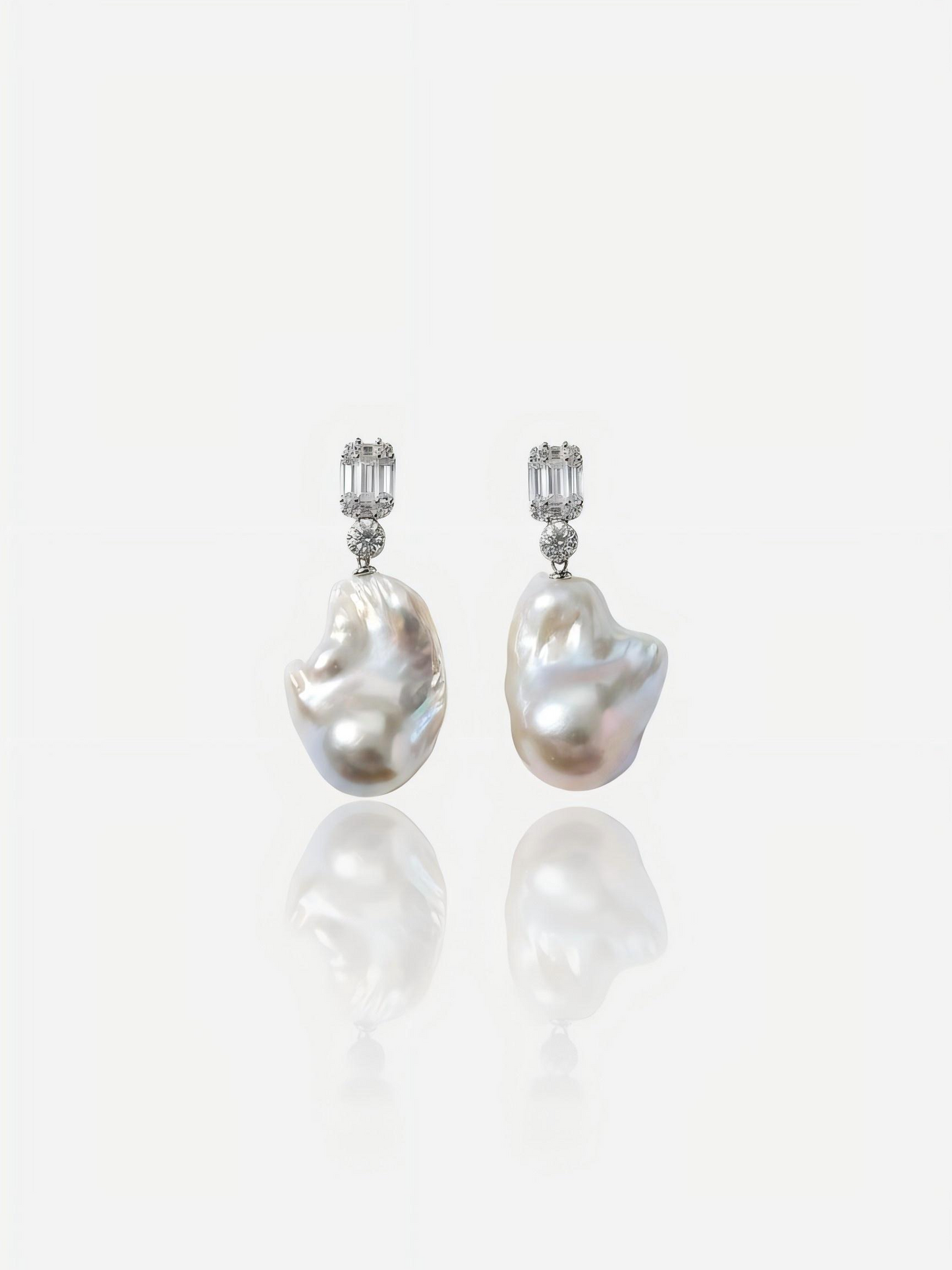 Close-up of Pearltide Lumina geometric baroque pearl jewelry earrings featuring emerald-cut cubic zirconia studs and massive organic pearls on a white reflective background, elegant modern bridal pearl jewelry.