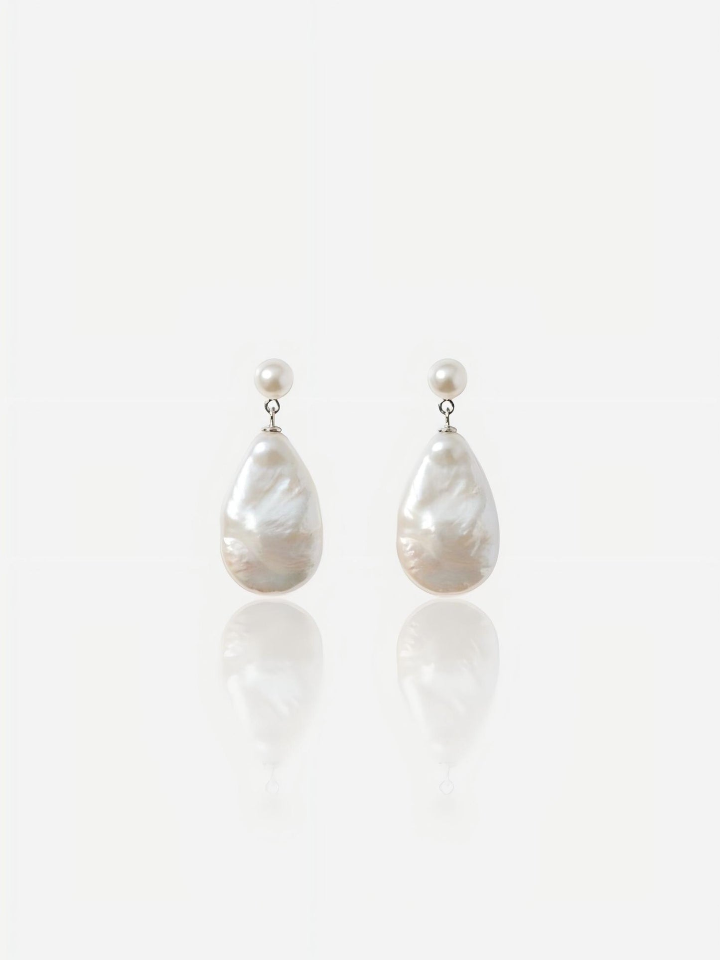 Close-up of Pearltide Odessa teardrop baroque pearl jewelry earrings featuring small round pearl studs and large pear-shaped waterdrop pearls on an S925 sterling silver setting against a white reflective background, elegant quiet luxury bridal jewelry.