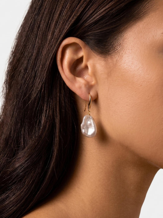 Close-up profile of a model wearing Pearltide 14K gold-filled sculptural baroque pearl drop earrings, highlighting the high-luster and elegant drape.
