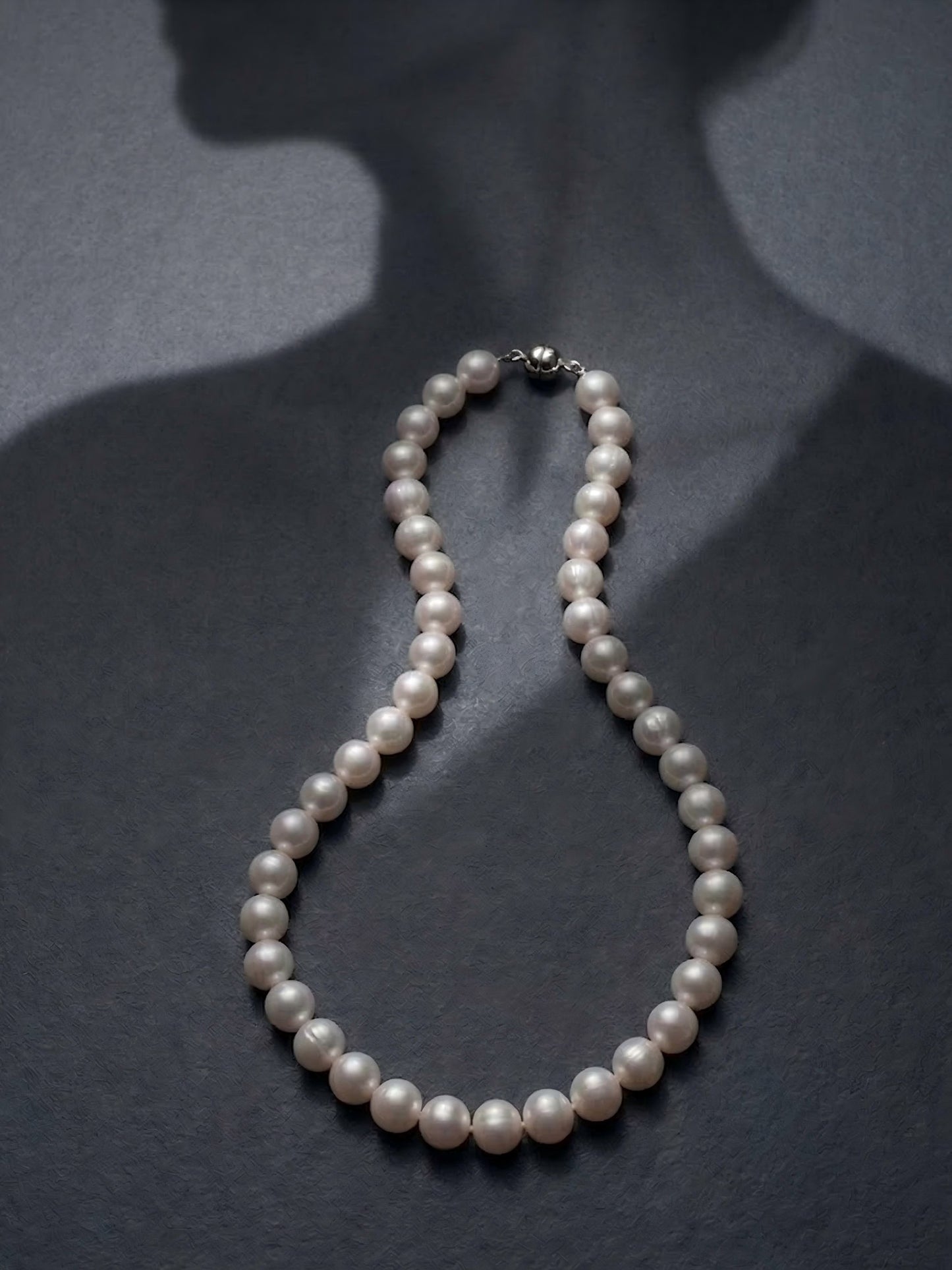 Classic round pearl necklace showcased on a dark silhouette, emphasizing a timeless, Old Money aesthetic.