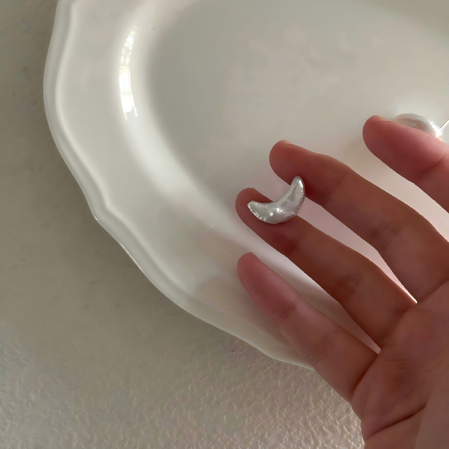 Hand holding a small, organic crescent moon pearl earring, showing the natural texture and luster.
