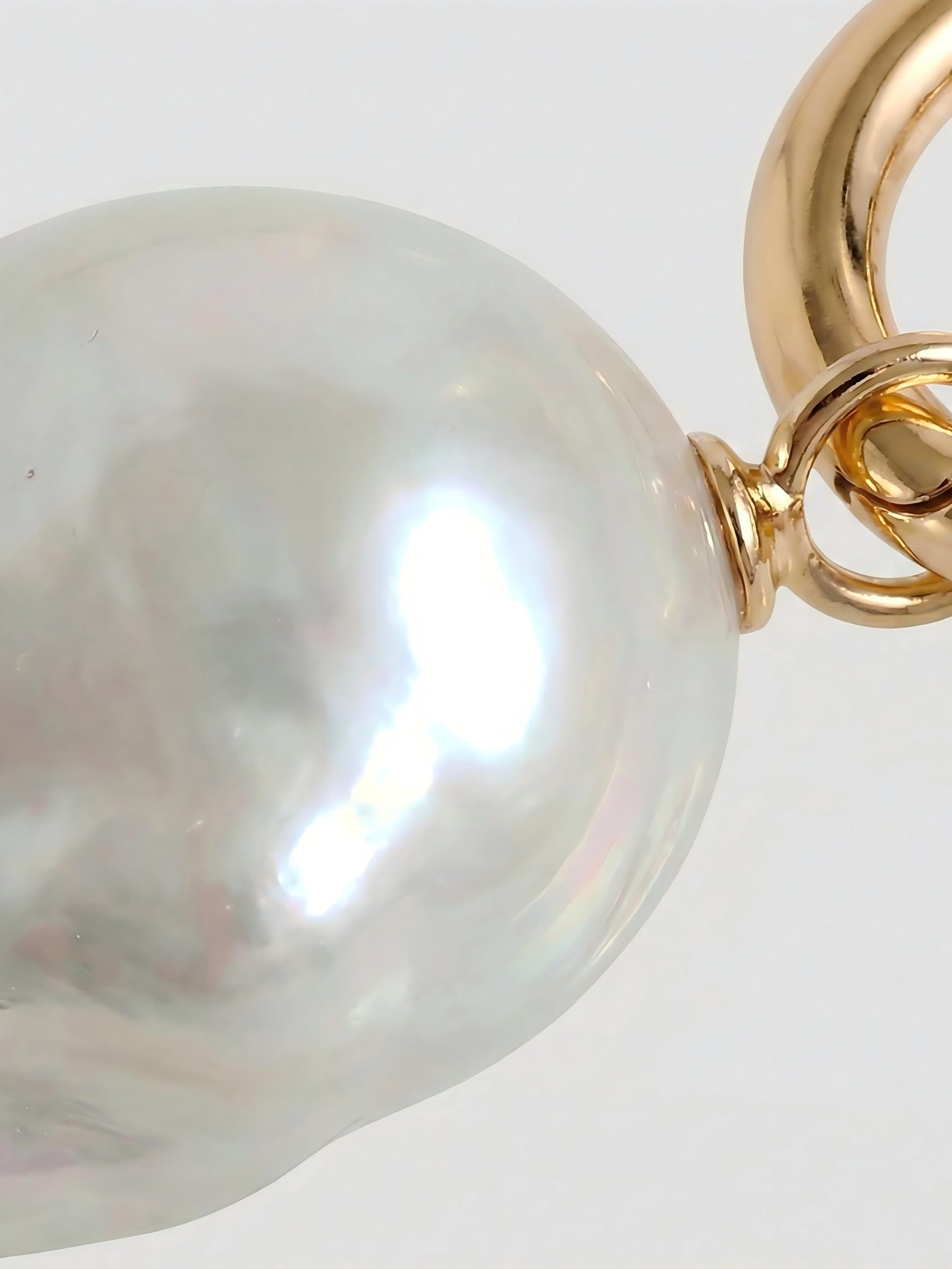 Macro close-up of a radiant natural baroque pearl attached to a polished 14k gold hoop, highlighting the gemstone's unique organic texture and high luster.
