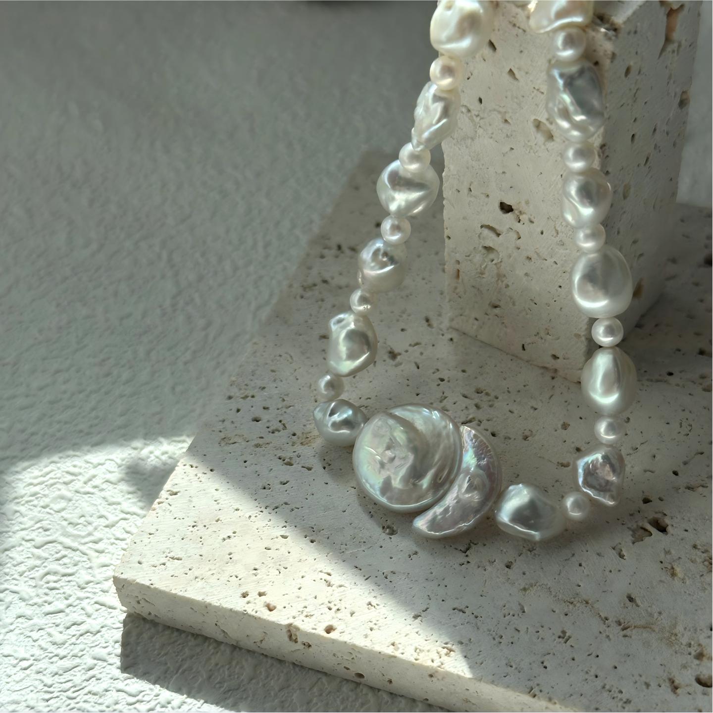 Close-up detail of the necklace centerpiece showing a large round pearl nestled against a crescent-shaped baroque pearl.