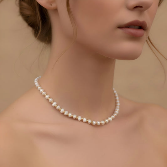 A model wearing the gold bead and pearl station necklace layered with a white shirt, showing the dainty choker length on the neck.