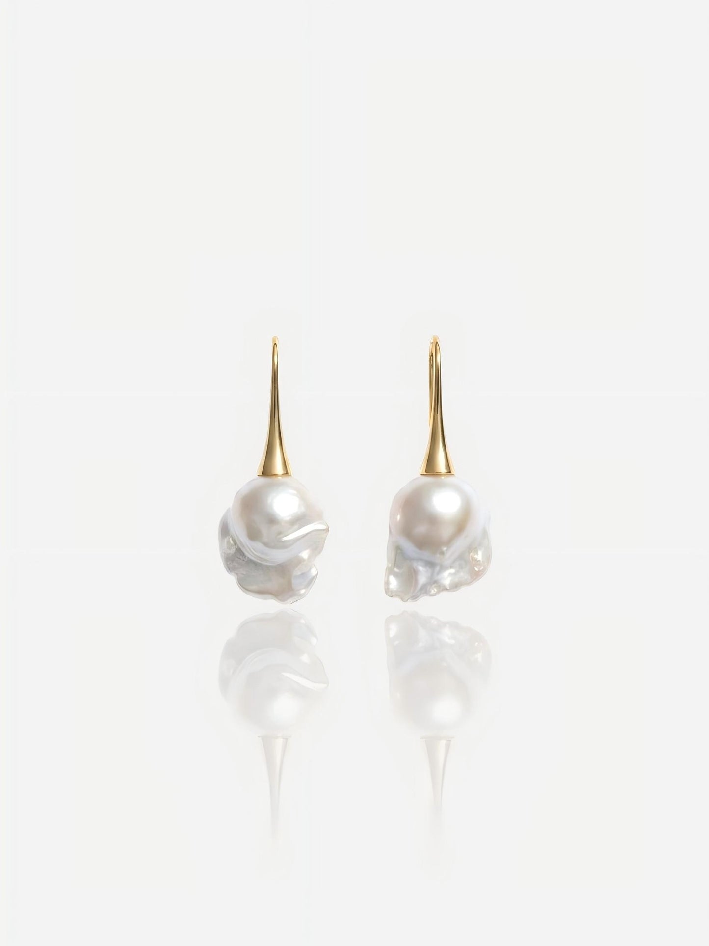 Close-up of Pearltide Aurelia baroque pearl jewelry earrings featuring sleek 14K gold-filled tapered hooks and massive lustrous organic pearls on a white reflective background, perfect for a modern bridal or resort luxury look.