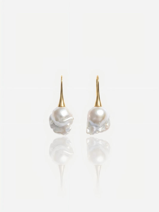 Close-up of Pearltide Aurelia baroque pearl jewelry earrings featuring sleek 14K gold-filled tapered hooks and massive lustrous organic pearls on a white reflective background, perfect for a modern bridal or resort luxury look.