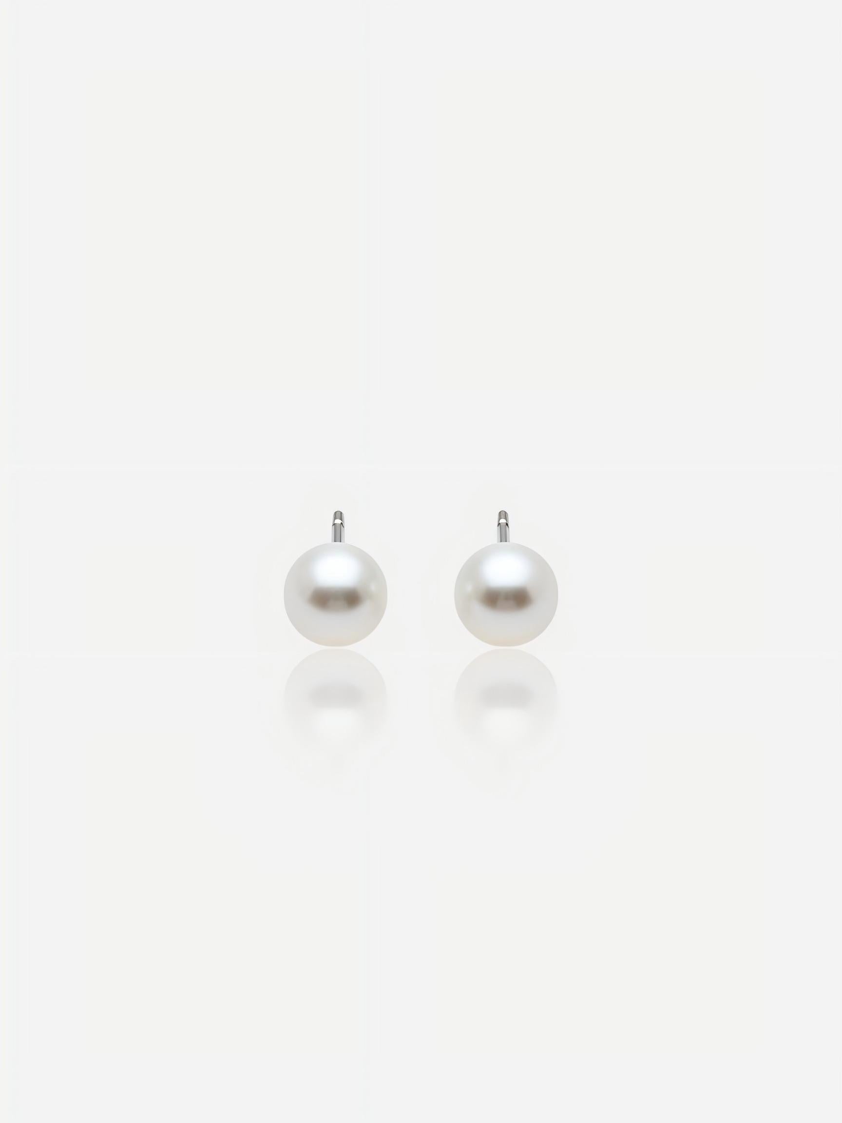 Close-up of Pearltide Aurora flawless round pearl jewelry earrings with brilliant Akoya-like mirror luster and S925 sterling silver settings on a white background with soft reflections, elegant minimalist bridal jewelry.