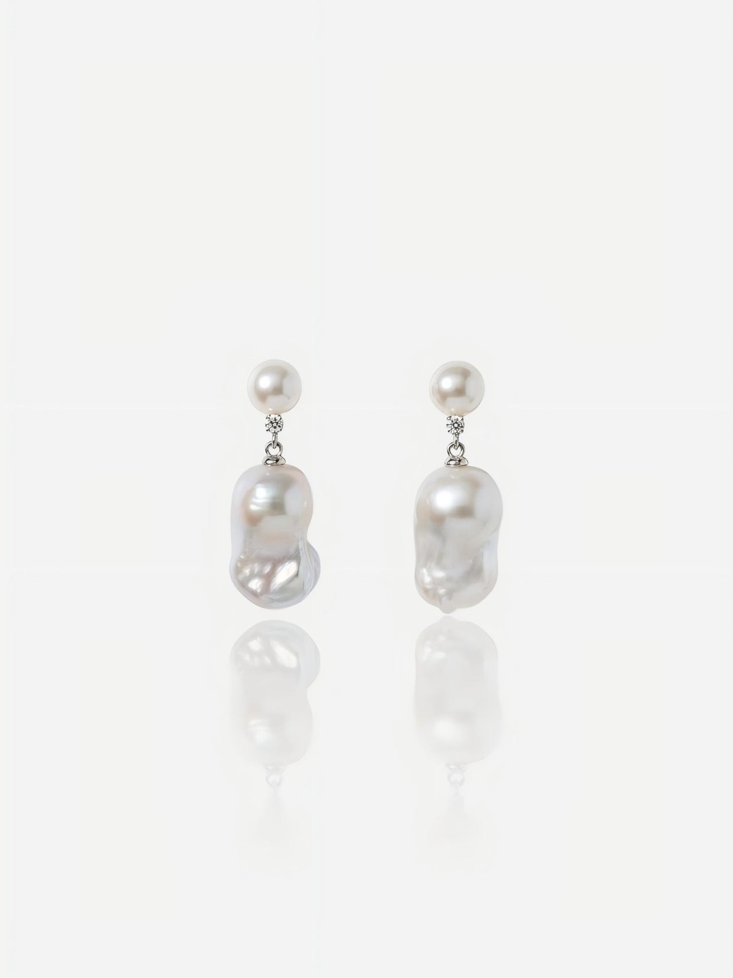 Close-up of Pearltide Celeste petite baroque pearl jewelry earrings featuring small round pearl studs, brilliant cubic zirconia links, and dainty organic drops on a white reflective background, elegant minimalist pearl jewelry.