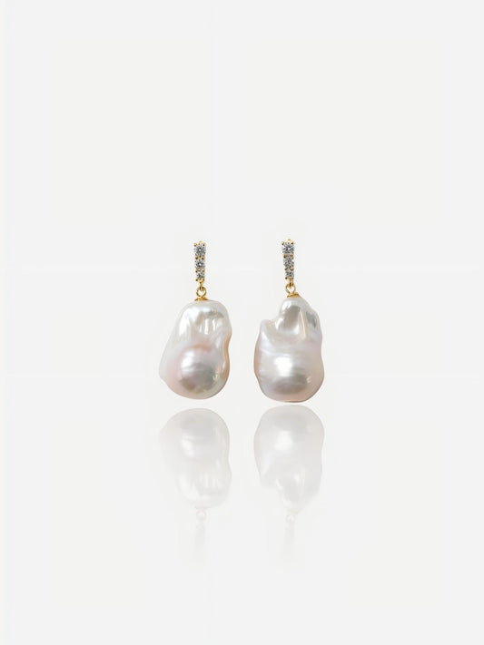 Close-up of Pearltide Elysian Rose baroque pearl jewelry earrings featuring sparkling cubic zirconia pavé bars and massive organic pearls with an iridescent rose luster on a white reflective background, elegant modern bridal jewelry.