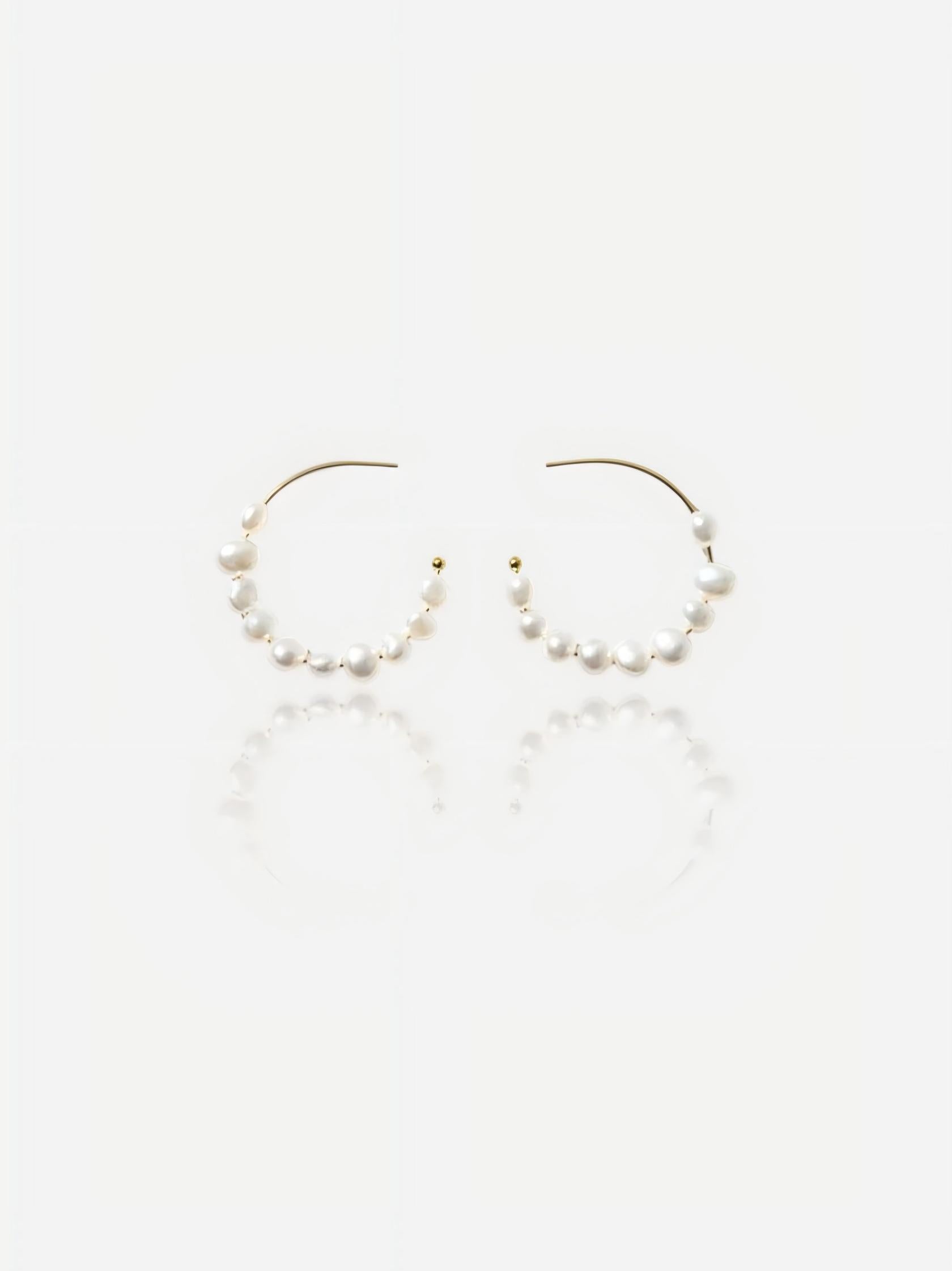 Top-down view of Pearltide Isla organic hoop pearl jewelry earrings featuring dainty gold C-hoops threaded with petite white baroque pearls on a textured beige backdrop, elegant minimalist resort jewelry.