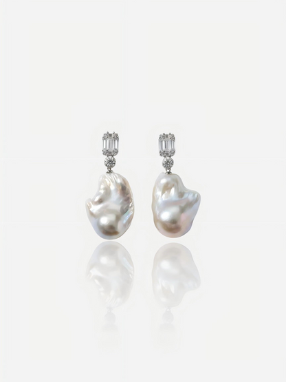 Close-up of Pearltide Lumina geometric baroque pearl jewelry earrings featuring emerald-cut cubic zirconia studs and massive organic pearls on a white reflective background, elegant modern bridal pearl jewelry.
