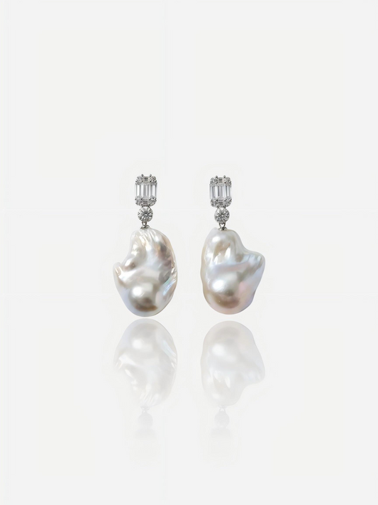 Close-up of Pearltide Lumina geometric baroque pearl jewelry earrings featuring emerald-cut cubic zirconia studs and massive organic pearls on a white reflective background, elegant modern bridal pearl jewelry.