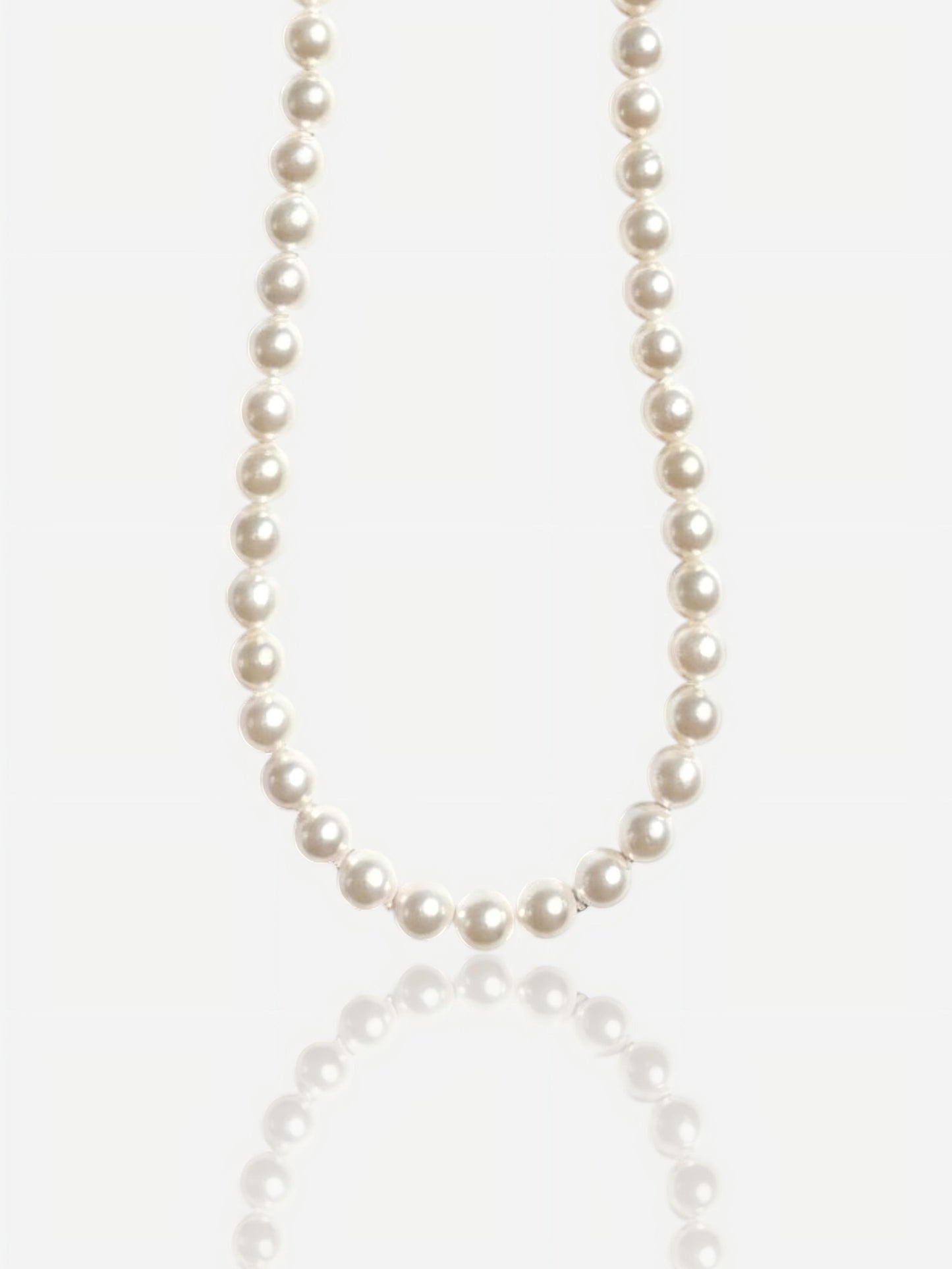 Close-up of Pearltide Eternal round pearl necklace with S925 sterling silver clasp on a white background with a soft reflection, luxury bridal jewelry.