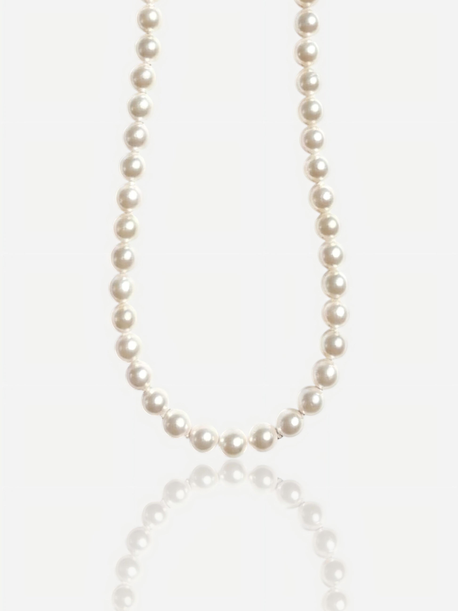 Close-up of Pearltide Eternal round pearl necklace with S925 sterling silver clasp on a white background with a soft reflection, luxury bridal jewelry.