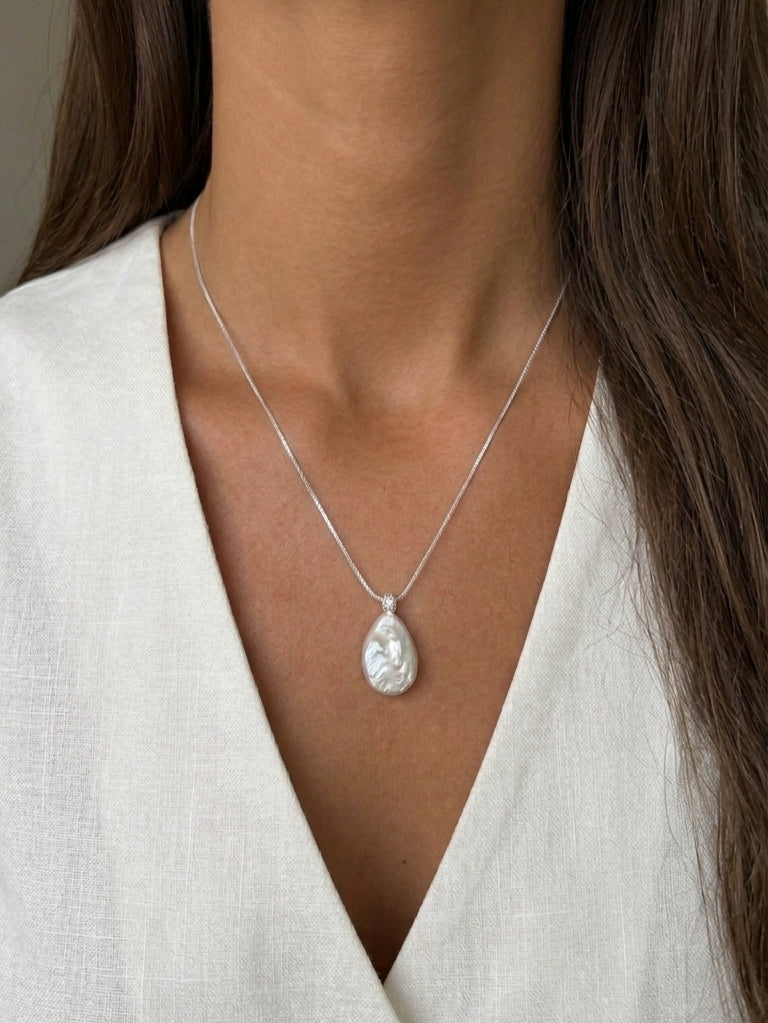 Close-up profile of a model with glowing tan skin wearing a delicate minimalist teardrop baroque pearl pendant necklace, showcasing high-luster, elegant bridal jewelry.