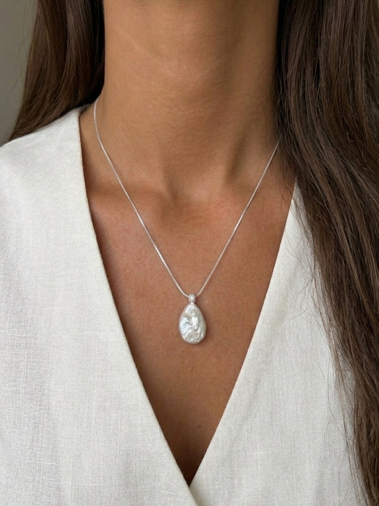 Close-up profile of a model with glowing tan skin wearing a delicate minimalist teardrop baroque pearl pendant necklace, showcasing high-luster, elegant bridal jewelry.