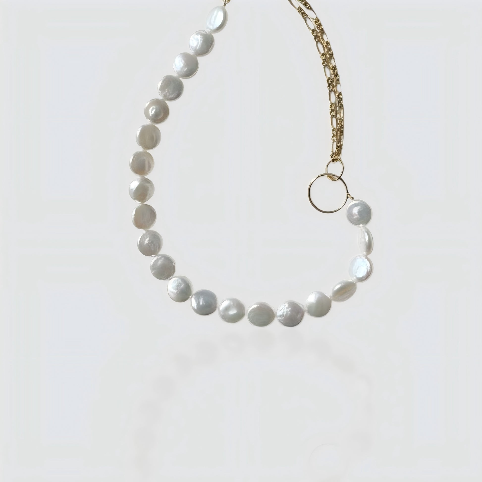 Studio shot of a half-pearl, half-chain necklace featuring flat coin pearls and a gold link chain connected by a ring.