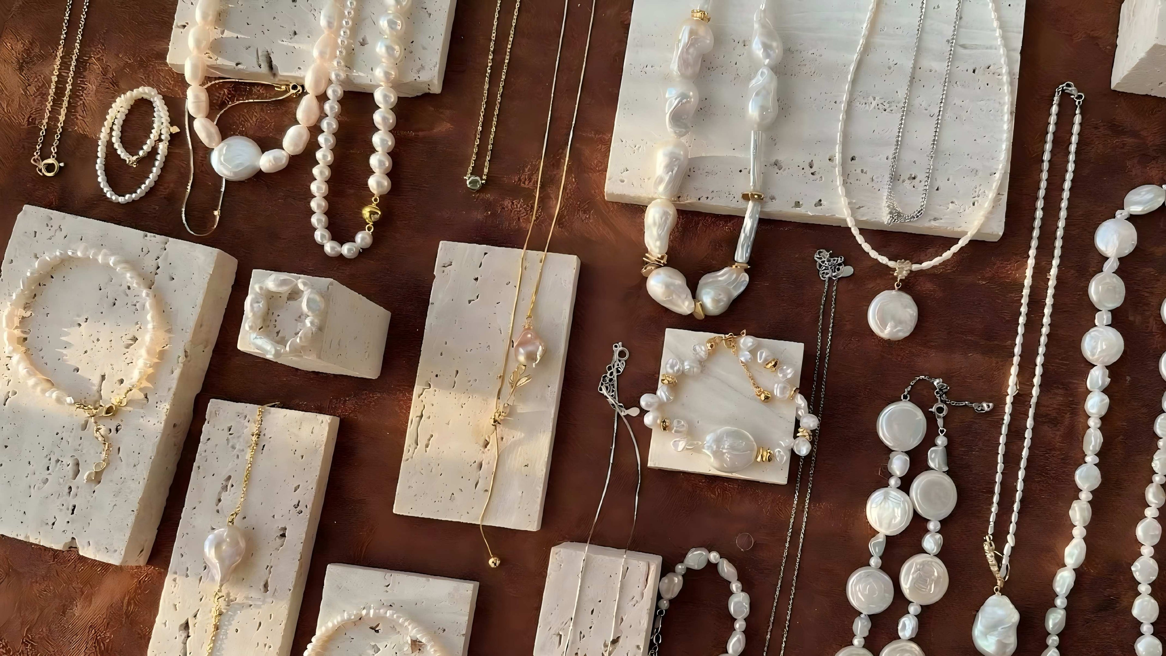 Collection of baroque pearl necklaces and bracelets displayed on stone blocks with text "Nature's Art, Wearable Elegance".