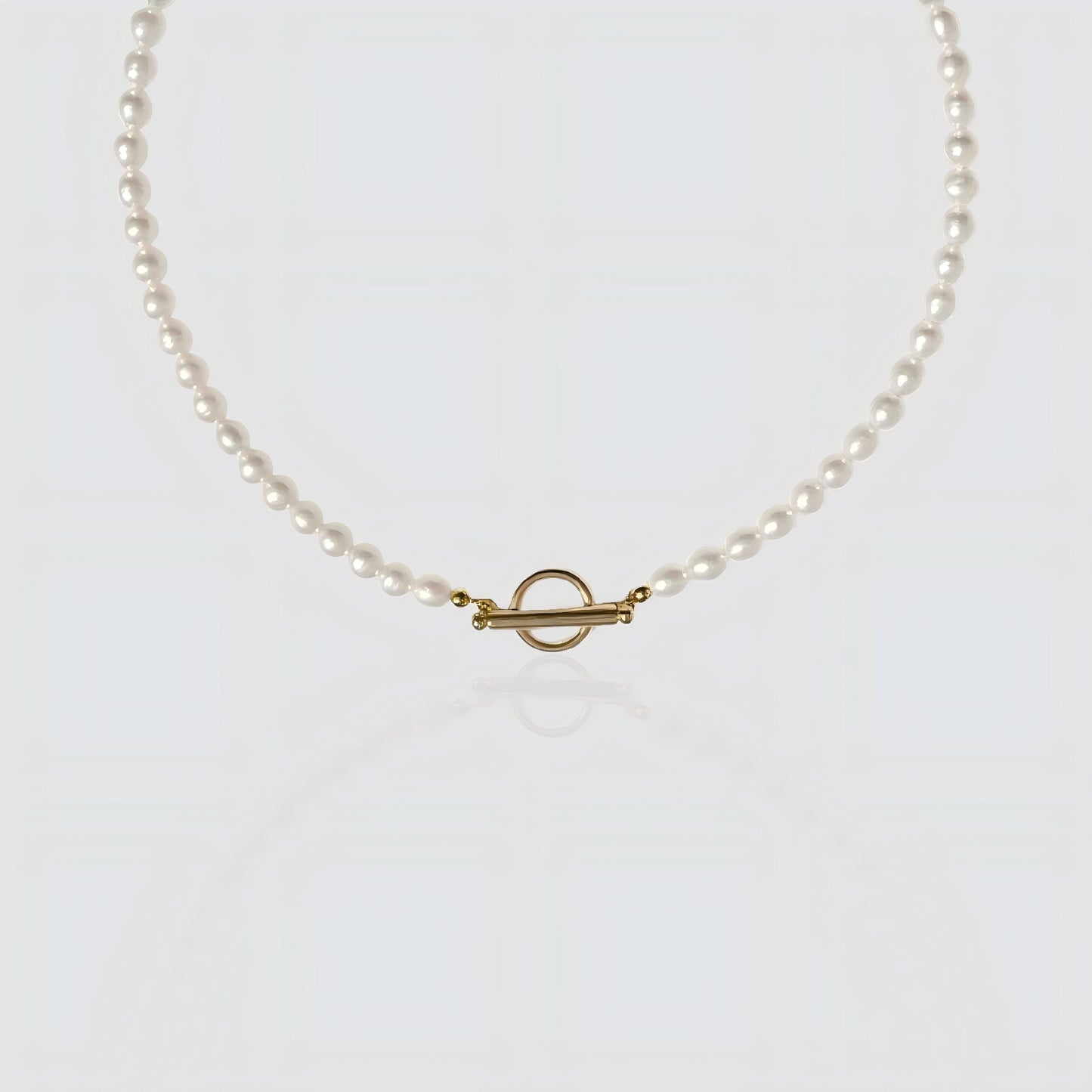 A strand of white freshwater pearls laid flat on a white background, featuring a minimalist gold toggle clasp closure.