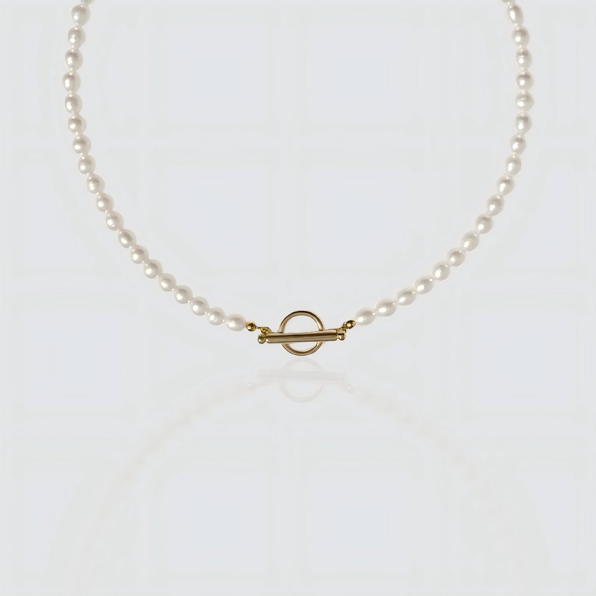 A strand of white freshwater pearls laid flat on a white background, featuring a minimalist gold toggle clasp closure.
