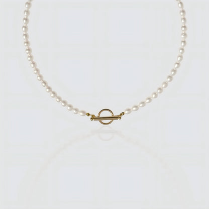 A strand of white freshwater pearls laid flat on a white background, featuring a minimalist gold toggle clasp closure.