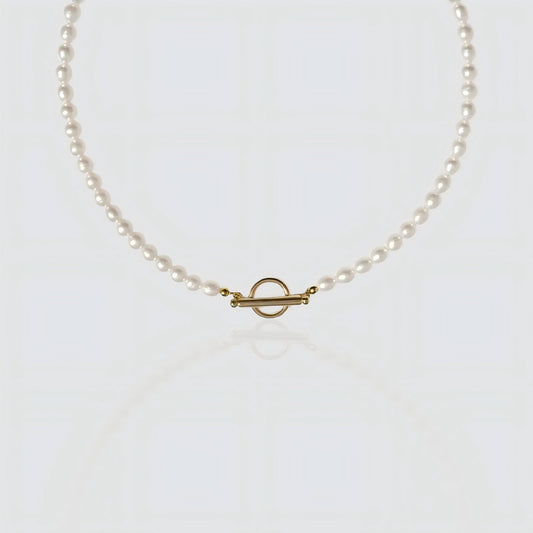 A strand of white freshwater pearls laid flat on a white background, featuring a minimalist gold toggle clasp closure.