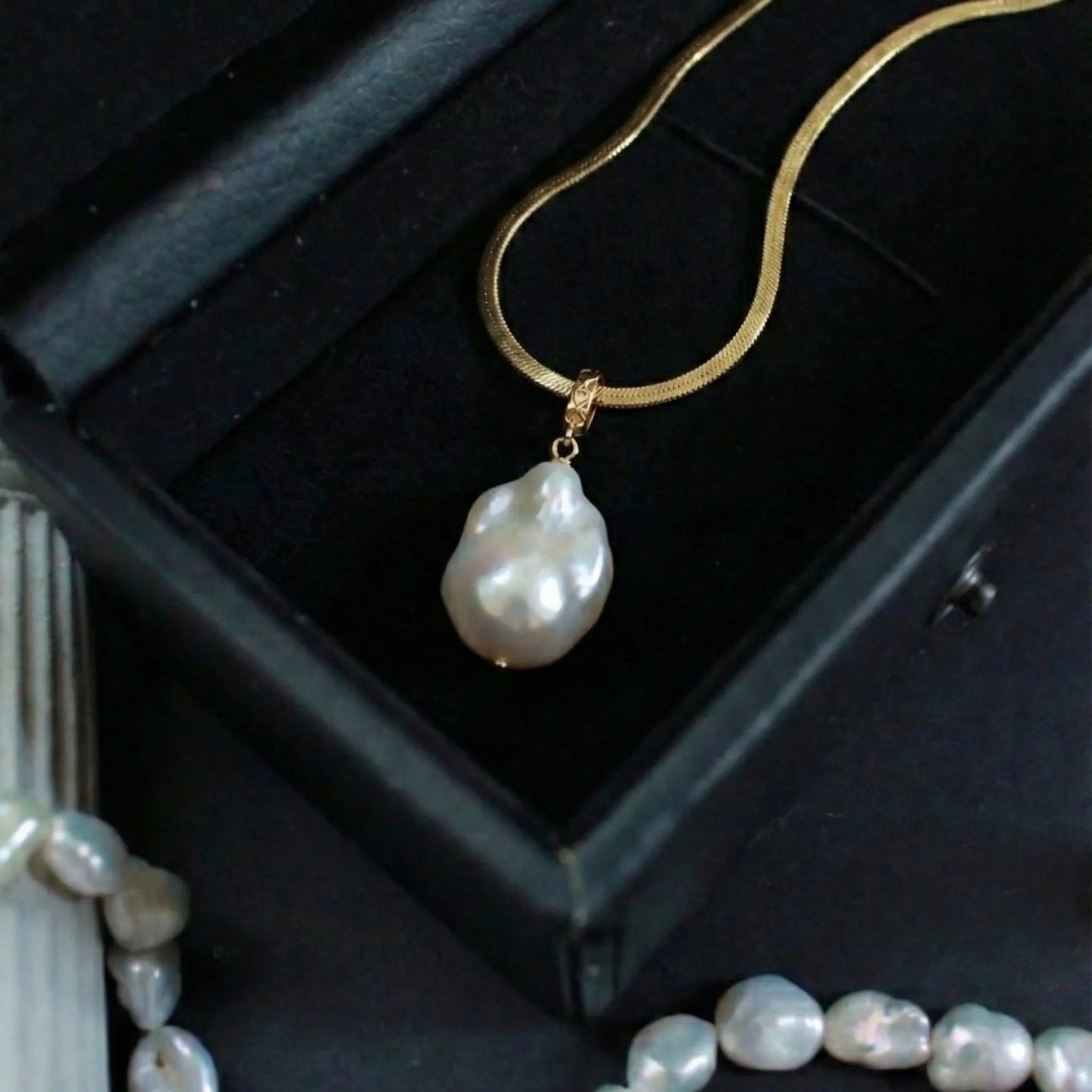 Close-up detail showing the luster of the irregular baroque pearl pendant hanging from the flat gold herringbone chain.