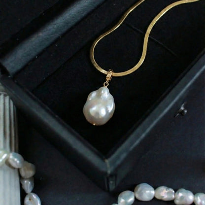 Close-up detail showing the luster of the irregular baroque pearl pendant hanging from the flat gold herringbone chain.
