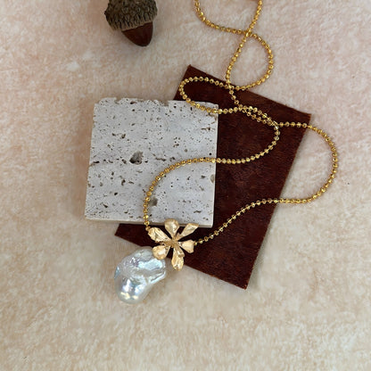 Close-up detail showing the intricate gold flower cap sitting on top of a natural white baroque pearl.