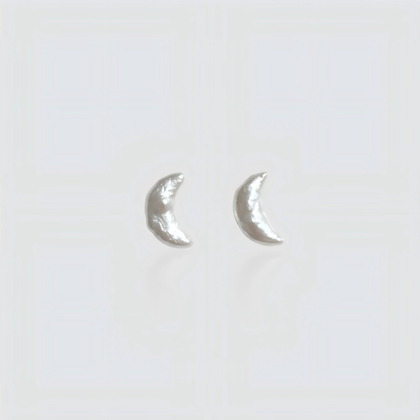 Pair of minimalist crescent moon-shaped baroque pearl stud earrings isolated on a white background.