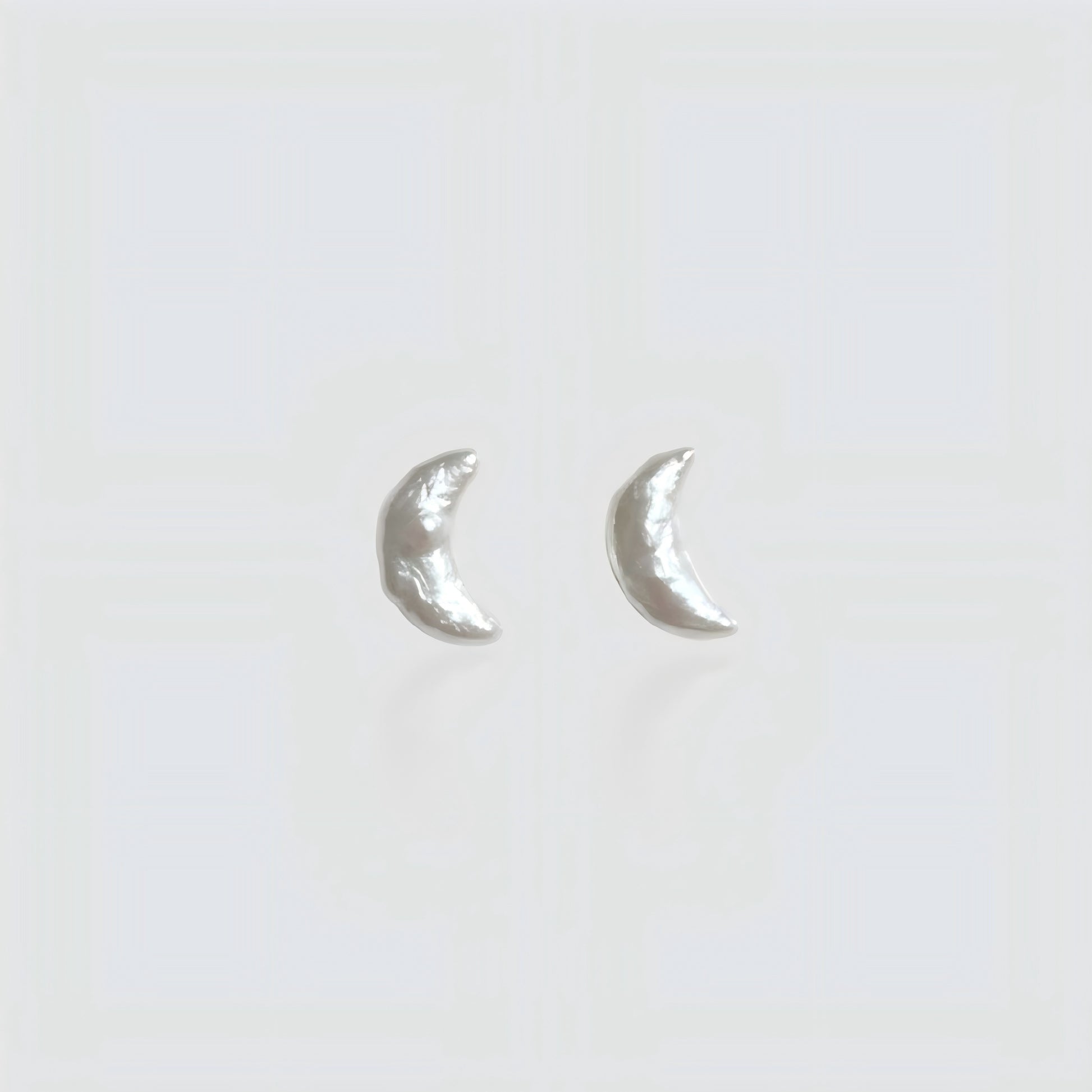 Pair of minimalist crescent moon-shaped baroque pearl stud earrings isolated on a white background.