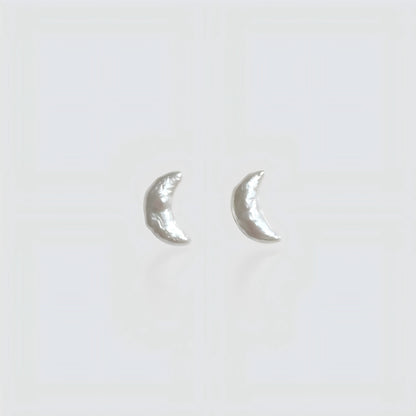 Pair of minimalist crescent moon-shaped baroque pearl stud earrings isolated on a white background.