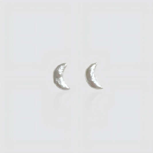 Pair of minimalist crescent moon-shaped baroque pearl stud earrings isolated on a white background.