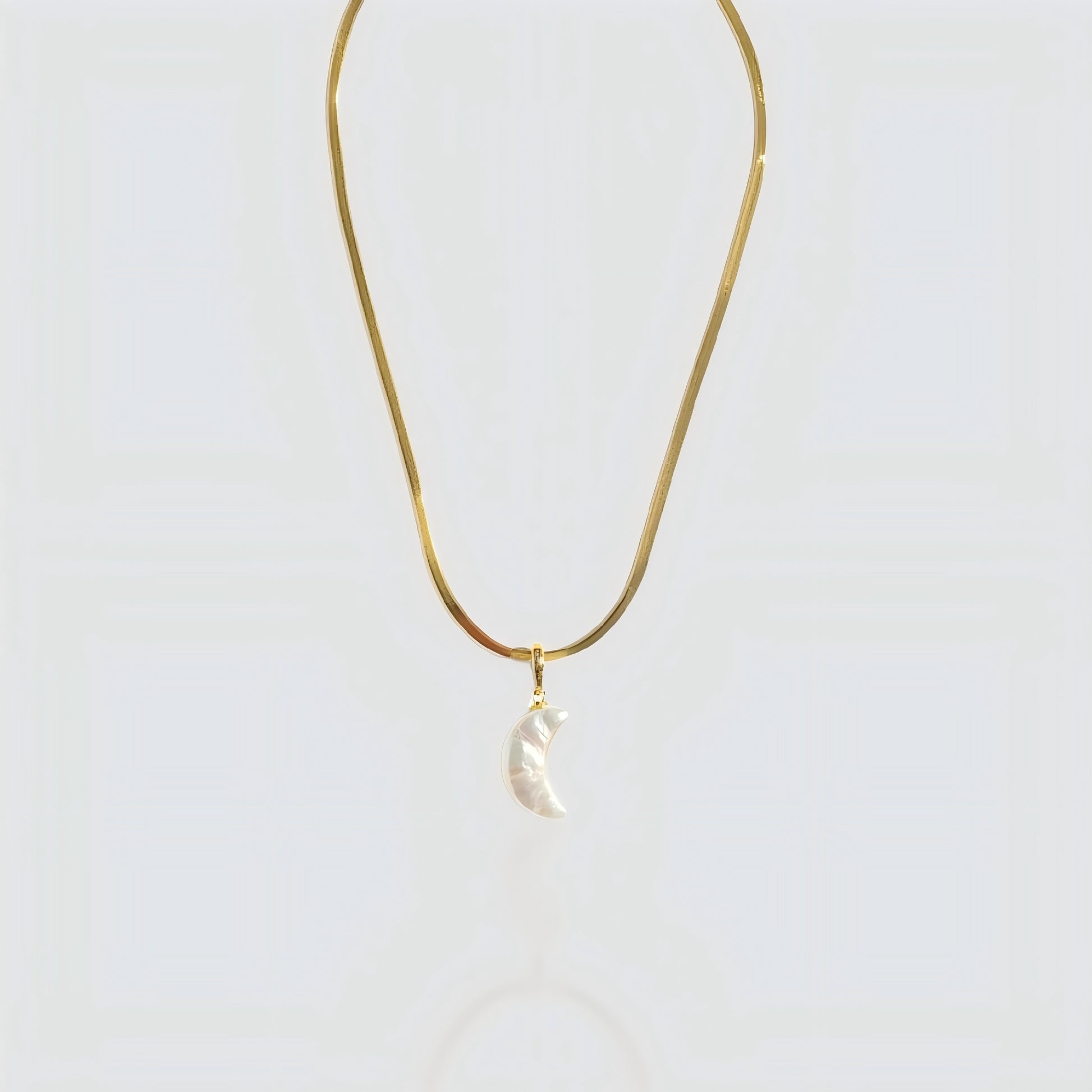 Studio shot of a white pearl crescent moon pendant attached to a flat gold snake chain on a grey background.