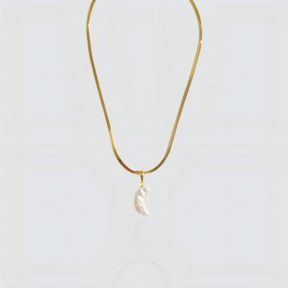 Studio shot of a white pearl crescent moon pendant attached to a flat gold snake chain on a grey background.