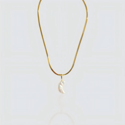Studio shot of a white pearl crescent moon pendant attached to a flat gold snake chain on a grey background.