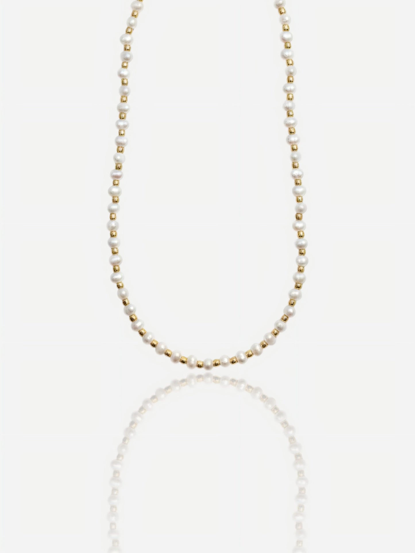 Dainty Pearltide Maya necklace with alternating tiny white rice pearls and 14K gold beads on a white background with a soft reflection, elegant daily wear jewelry for a bridesmaid gift.