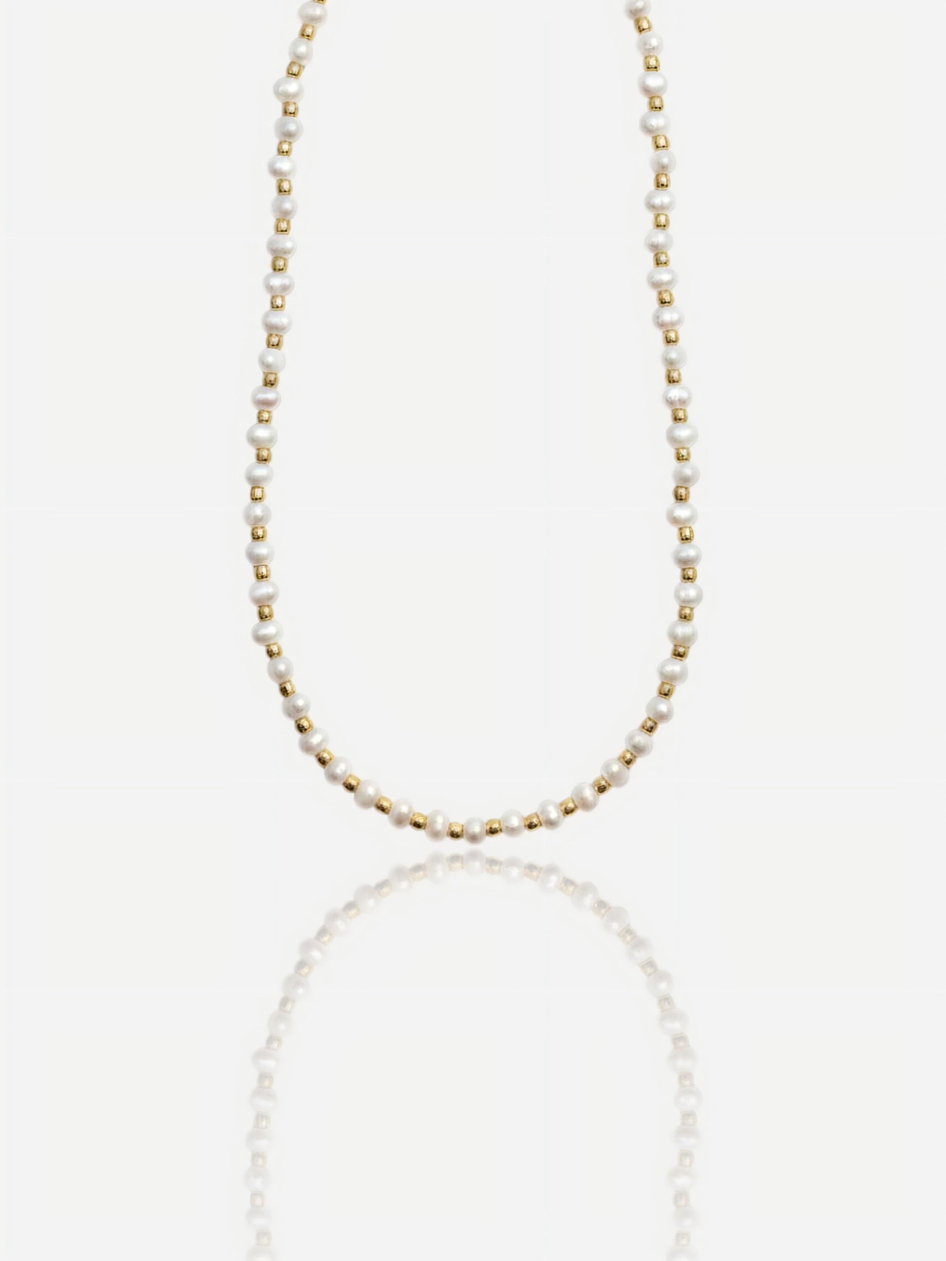 Dainty Pearltide Maya necklace with alternating tiny white rice pearls and 14K gold beads on a white background with a soft reflection, elegant daily wear jewelry for a bridesmaid gift.