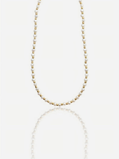 Dainty Pearltide Maya necklace with alternating tiny white rice pearls and 14K gold beads on a white background with a soft reflection, elegant daily wear jewelry for a bridesmaid gift.