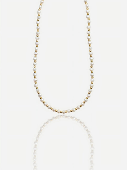 Dainty Pearltide Maya necklace with alternating tiny white rice pearls and 14K gold beads on a white background with a soft reflection, elegant daily wear jewelry for a bridesmaid gift.