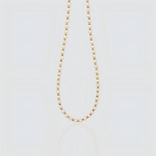 Studio product shot of a delicate necklace featuring alternating small white freshwater pearls and gold beads on a light grey background.
