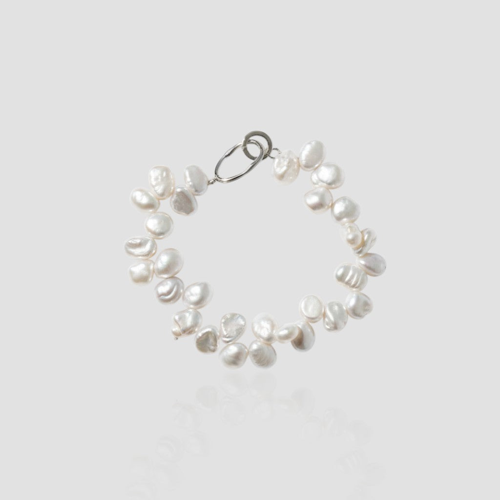 Studio shot of a chunky white pearl bracelet with a cluster design and silver oval clasp on a light grey background.