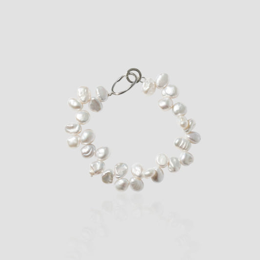 Studio shot of a chunky white pearl bracelet with a cluster design and silver oval clasp on a light grey background.