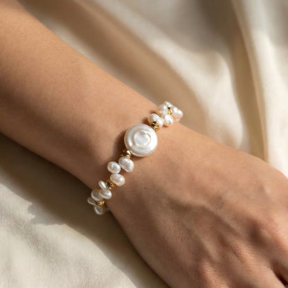Woman's wrist wearing an elegant coin pearl bracelet with gold accents, styled with a warm-toned sweater to highlight the gold details.