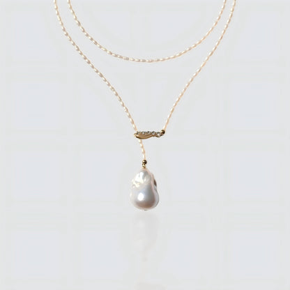 A studio shot of a dainty seed pearl necklace with a gold crystal bar and a baroque pearl drop, isolated on a white background.