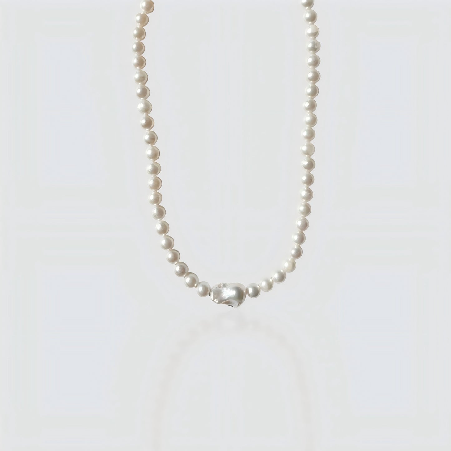 Studio shot of a large pearl strand necklace culminating in a massive, metallic-luster baroque Edison pearl centerpiece on a textured stone surface.