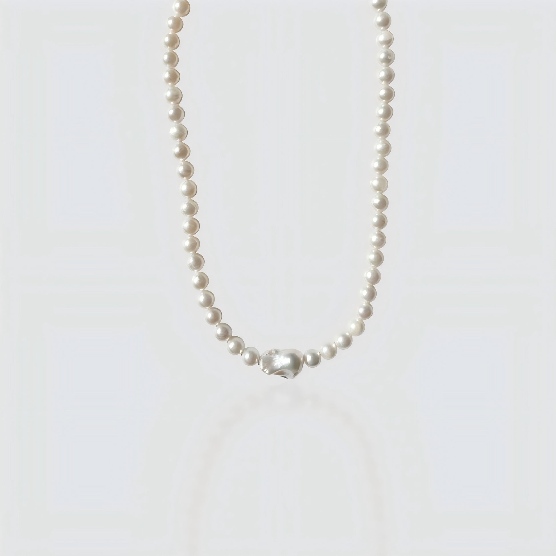 Studio shot of a large pearl strand necklace culminating in a massive, metallic-luster baroque Edison pearl centerpiece on a textured stone surface.