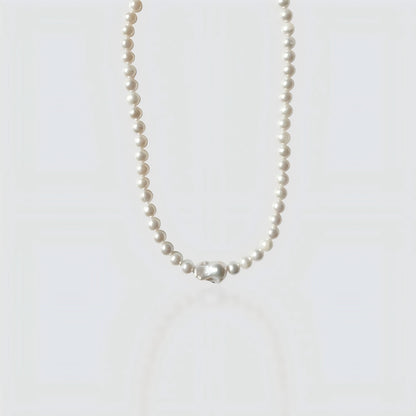 Studio shot of a large pearl strand necklace culminating in a massive, metallic-luster baroque Edison pearl centerpiece on a textured stone surface.