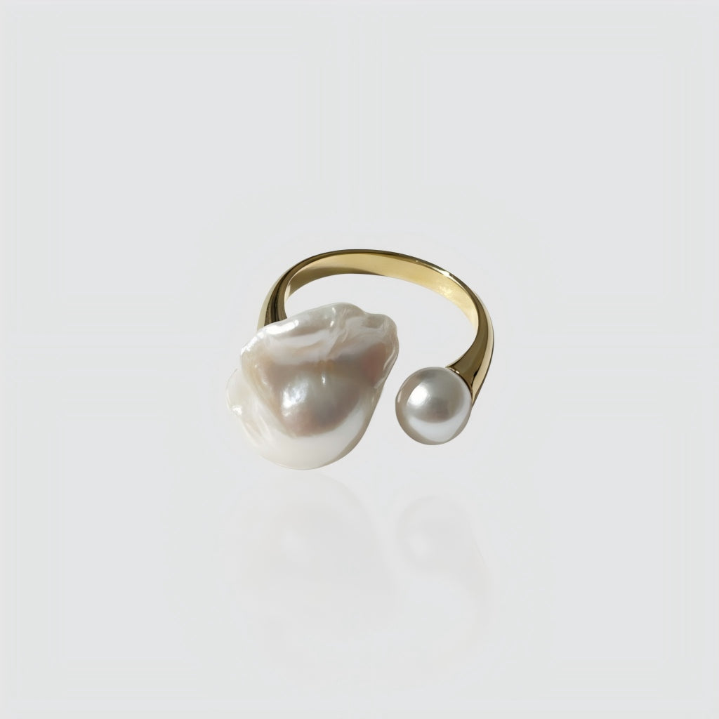 Woman's hand wearing a gold open ring with one large baroque pearl and one small round pearl.